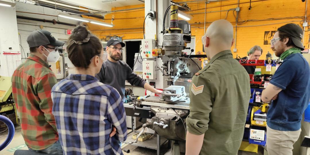 4 people listening and watching Brandon, the instructor, indicating something on the Bridgeport Mill